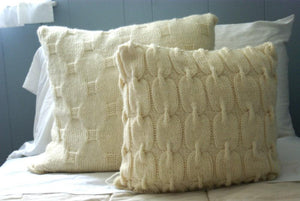 set of cable knit pillows shown sitting on a bed